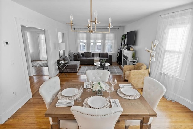 dining space featuring a healthy amount of sunlight, light wood-style flooring, baseboards, and a notable chandelier