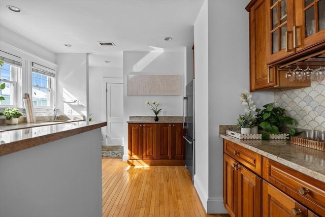 kitchen with light stone countertops, visible vents, glass insert cabinets, and brown cabinetry