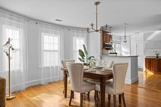 dining space featuring a chandelier, light wood-type flooring, visible vents, and baseboards