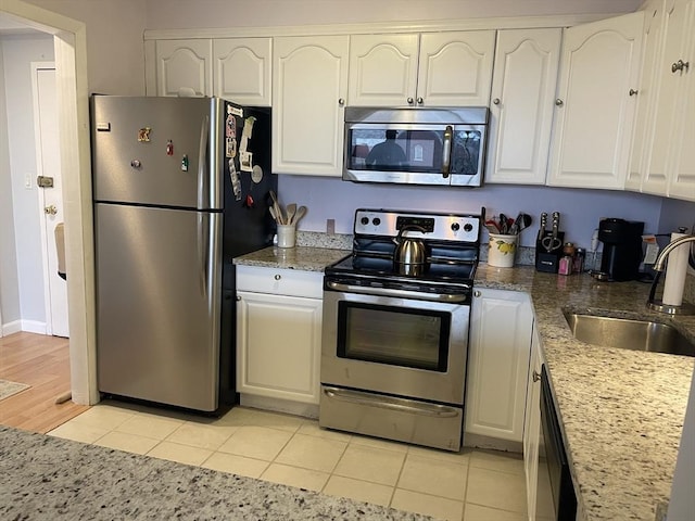 kitchen featuring a sink, stainless steel appliances, light tile patterned flooring, and white cabinetry