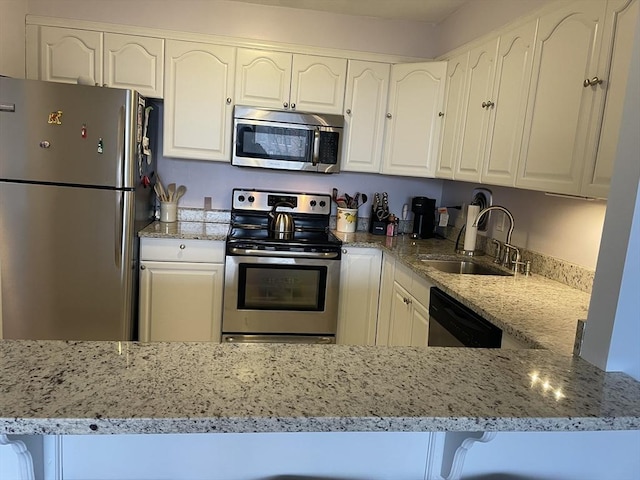 kitchen with light stone counters, a peninsula, a sink, stainless steel appliances, and white cabinetry