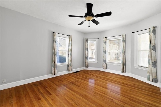 empty room featuring ceiling fan, wood-type flooring, and a wealth of natural light