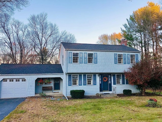 colonial inspired home with aphalt driveway, a front yard, a chimney, and an attached garage