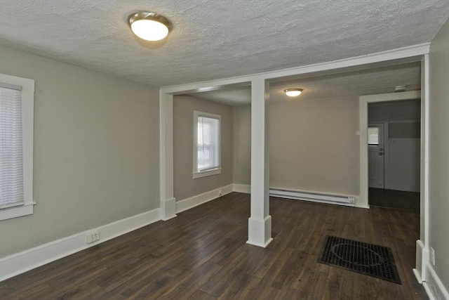 below grade area with visible vents, a baseboard heating unit, dark wood finished floors, and baseboards