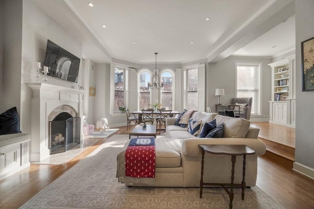 living room with built in shelves, light wood-type flooring, crown molding, and a notable chandelier