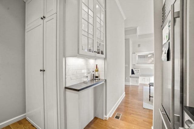 interior space with high end refrigerator, light wood-type flooring, tasteful backsplash, and white cabinetry