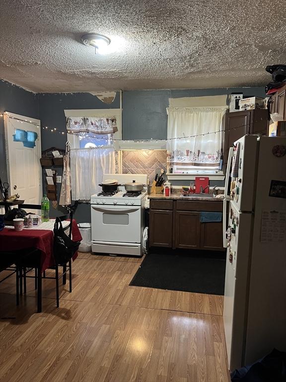 kitchen featuring a textured ceiling, white appliances, light hardwood / wood-style floors, and sink