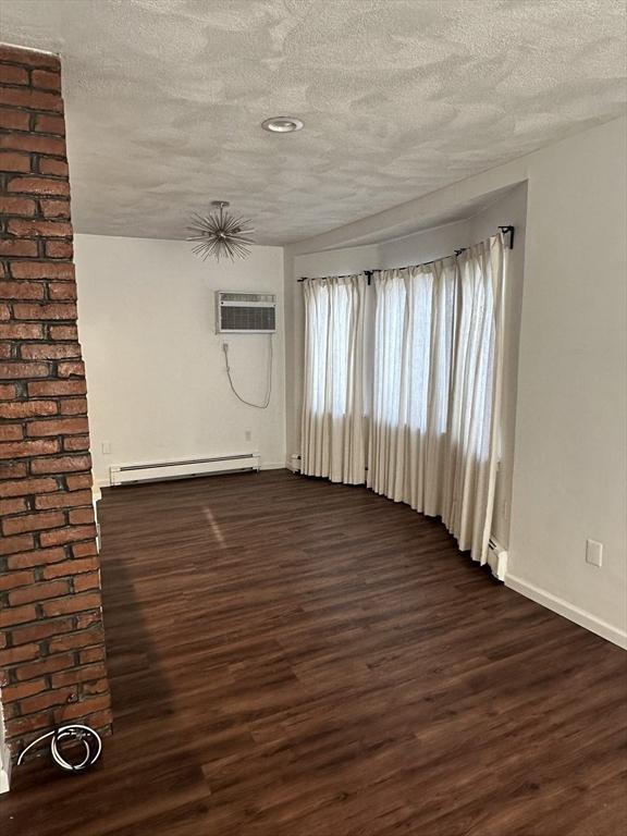 unfurnished room with dark hardwood / wood-style flooring, an AC wall unit, a textured ceiling, and baseboard heating