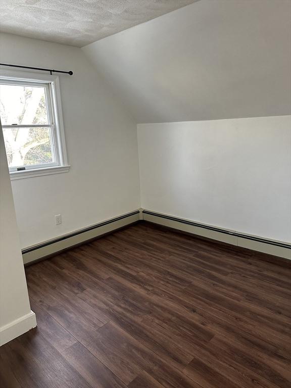 bonus room featuring vaulted ceiling, a textured ceiling, dark hardwood / wood-style flooring, and a baseboard radiator