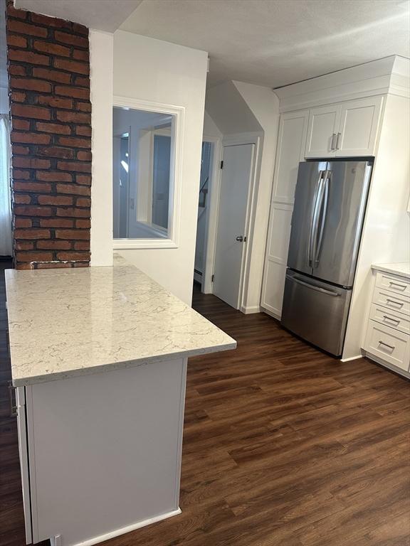 kitchen featuring light stone counters, stainless steel fridge, dark hardwood / wood-style flooring, and white cabinets