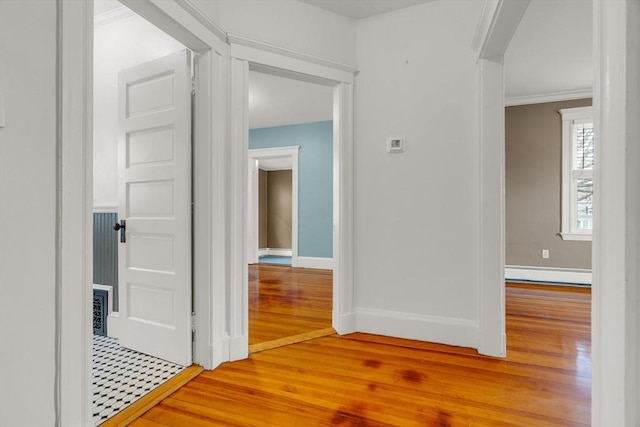 corridor featuring baseboard heating, wood-type flooring, and ornamental molding