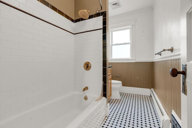 bathroom featuring a baseboard radiator, toilet, tiled shower / bath, and wooden walls