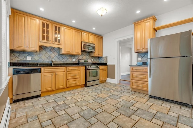 kitchen featuring appliances with stainless steel finishes, backsplash, baseboard heating, sink, and dark stone countertops