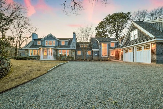 view of front of house featuring gravel driveway, an attached garage, a chimney, and a yard