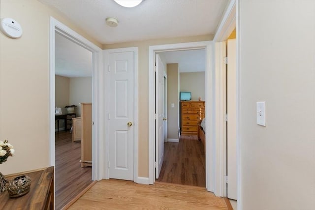 hallway featuring light wood finished floors and baseboards