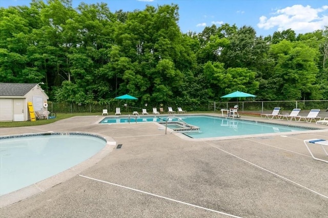 community pool with fence, a patio area, a hot tub, and an outdoor structure
