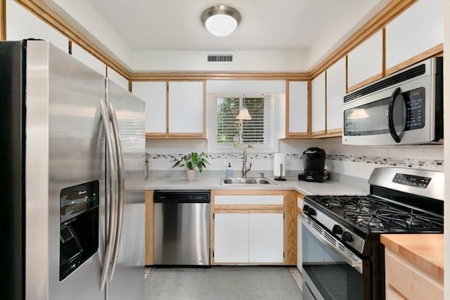 kitchen featuring appliances with stainless steel finishes, a sink, light countertops, and tasteful backsplash