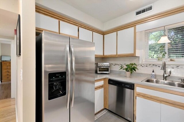 kitchen with stainless steel appliances, a sink, light countertops, white cabinets, and backsplash