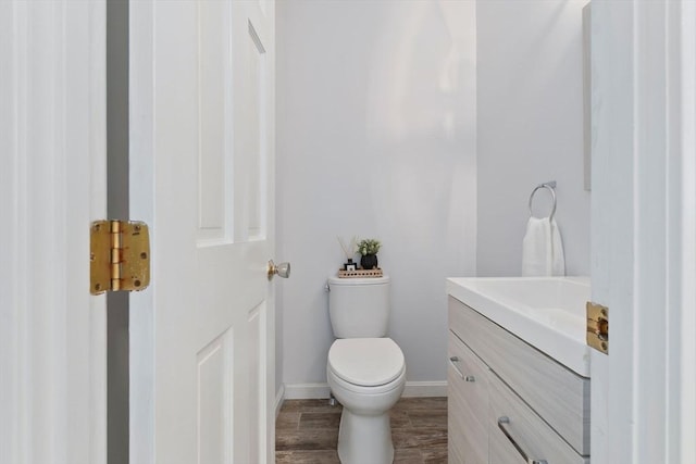half bathroom featuring toilet, vanity, baseboards, and wood finished floors