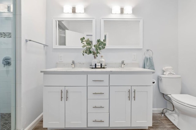 bathroom with toilet, a stall shower, baseboards, double vanity, and wood finished floors