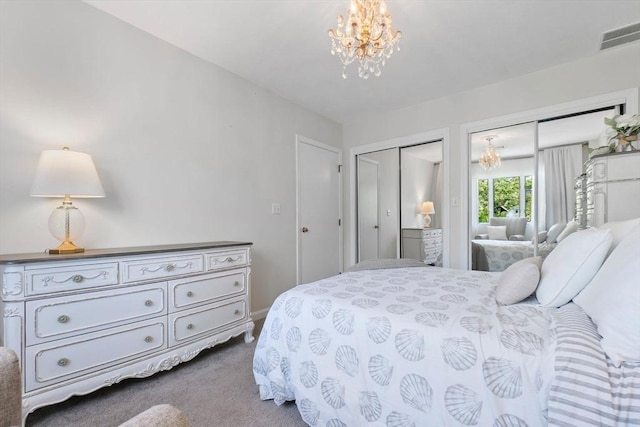 bedroom with two closets, a chandelier, and carpet flooring