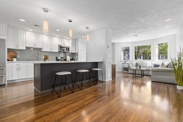 kitchen with stainless steel appliances, white cabinets, light countertops, a kitchen breakfast bar, and recessed lighting