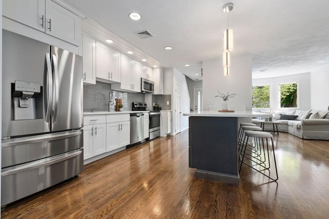 kitchen featuring appliances with stainless steel finishes, open floor plan, dark wood-style floors, light countertops, and a kitchen breakfast bar