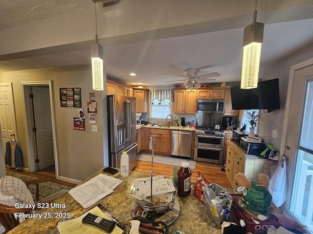 kitchen featuring high quality appliances, light wood-style floors, brown cabinets, light stone countertops, and decorative light fixtures