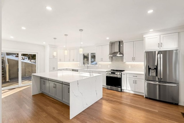 kitchen with appliances with stainless steel finishes, a center island, wall chimney range hood, and white cabinets