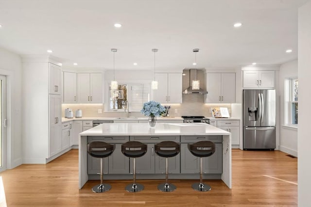 kitchen featuring wall chimney exhaust hood, stainless steel appliances, a kitchen island, and white cabinets