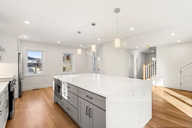 kitchen featuring pendant lighting, a spacious island, gray cabinetry, stainless steel appliances, and light hardwood / wood-style flooring