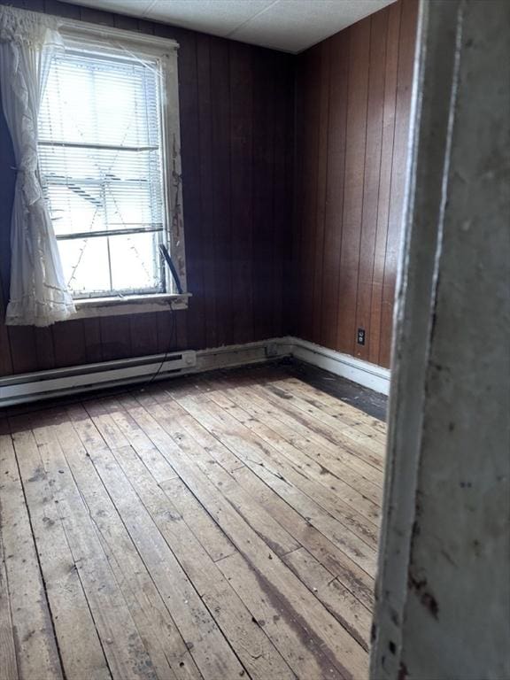 empty room with light wood-type flooring, baseboard heating, and wood walls