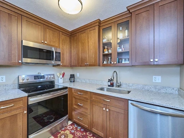 71 Princeton St Unit 305, Chelmsford, MA 01863 - kitchen featuring stainless steel appliances, a sink, brown cabinets, glass insert cabinets, and light stone counters