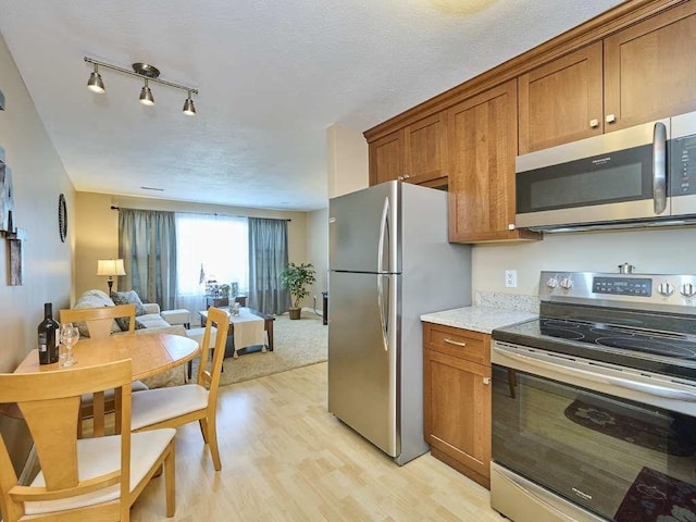 71 Princeton St Unit 305, Chelmsford, MA 01863 - kitchen featuring appliances with stainless steel finishes, brown cabinets, light wood-style flooring, open floor plan, and light stone countertops