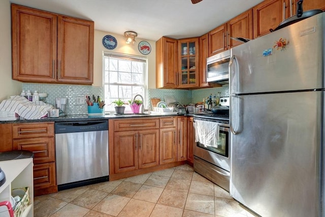 kitchen featuring dark stone countertops, appliances with stainless steel finishes, sink, light tile patterned floors, and tasteful backsplash