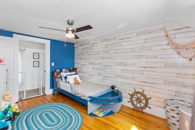 bedroom with ceiling fan, wooden walls, and wood finished floors