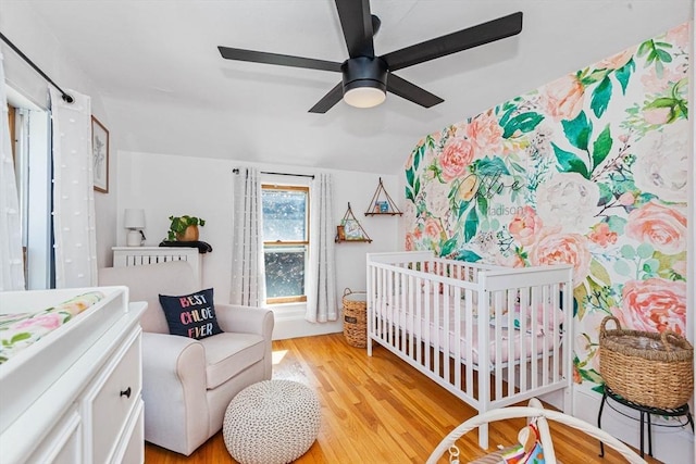 bedroom featuring a nursery area, ceiling fan, vaulted ceiling, and light wood-style flooring