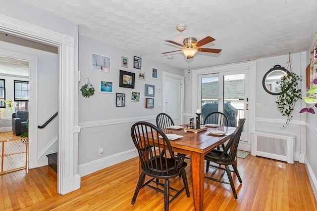 dining room with a textured ceiling, a ceiling fan, baseboards, light wood-type flooring, and radiator heating unit