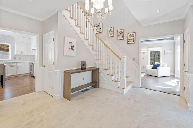 stairway with a chandelier, a decorative wall, wood finished floors, visible vents, and crown molding