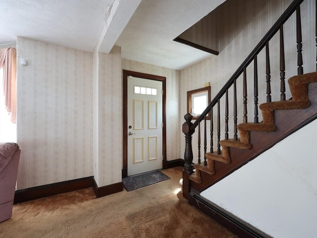 carpeted foyer entrance featuring baseboards, a textured ceiling, stairway, and wallpapered walls