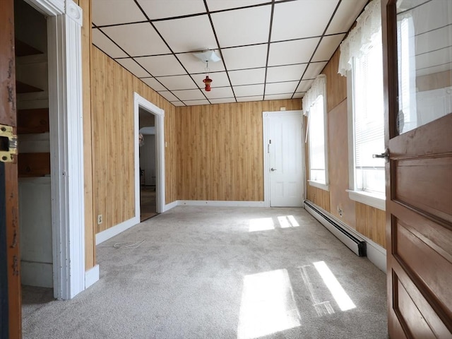 carpeted empty room featuring baseboards, a drop ceiling, a baseboard heating unit, and wooden walls