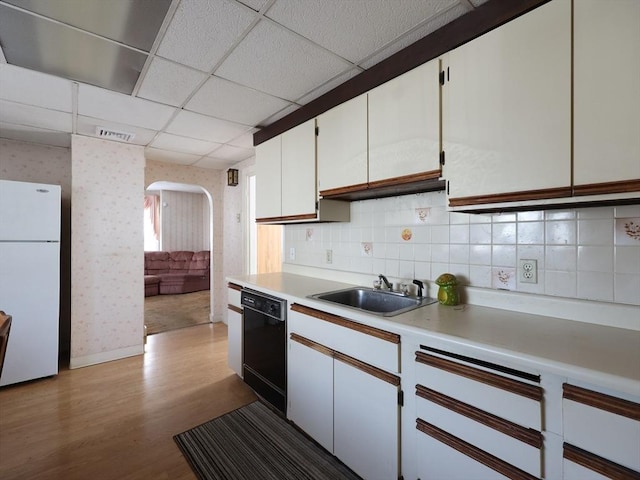 kitchen featuring arched walkways, dishwasher, a sink, light countertops, and freestanding refrigerator