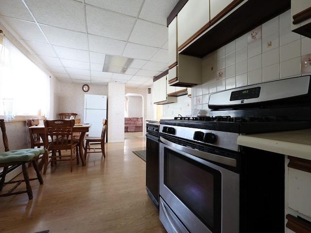 kitchen featuring white cabinets, light wood finished floors, arched walkways, stainless steel range with gas cooktop, and freestanding refrigerator