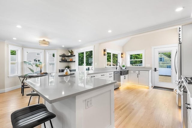 586 Lowell St, Peabody, MA 01960 - kitchen featuring appliances with stainless steel finishes, a breakfast bar, ornamental molding, white cabinets, and light wood-style floors