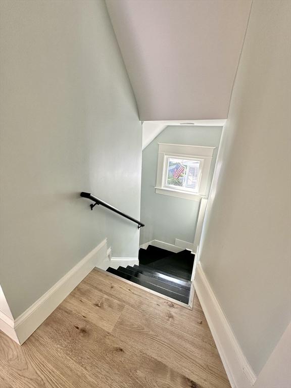 staircase featuring lofted ceiling, baseboards, and wood finished floors