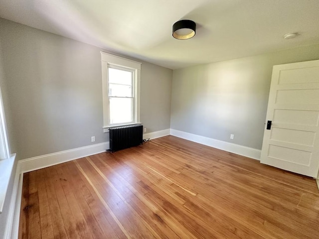 empty room featuring light wood-type flooring, baseboards, and radiator heating unit