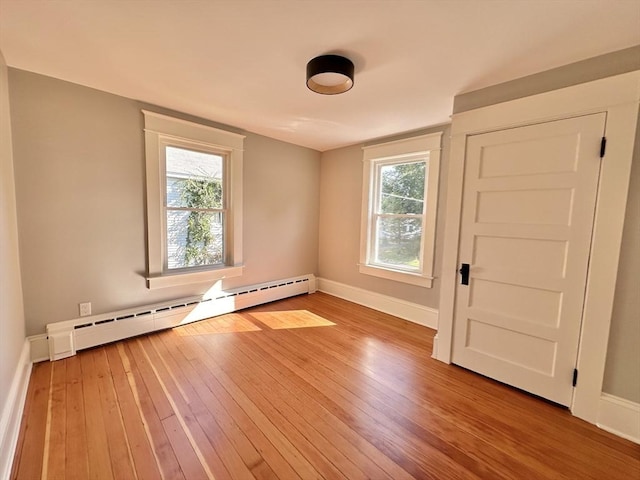 unfurnished room with a baseboard radiator, light wood-style flooring, and baseboards