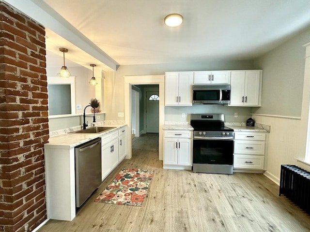 kitchen featuring light wood-style flooring, a sink, white cabinets, appliances with stainless steel finishes, and radiator