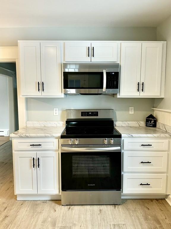 kitchen with appliances with stainless steel finishes, white cabinets, light wood-style floors, and light stone counters