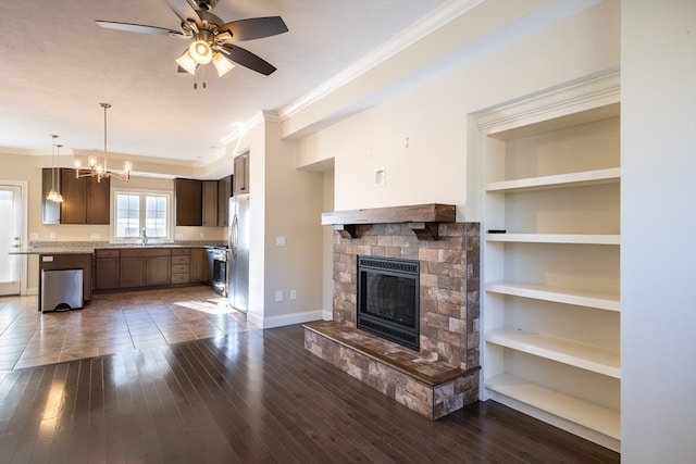 unfurnished living room featuring dark hardwood / wood-style flooring, ornamental molding, ceiling fan with notable chandelier, built in features, and a fireplace